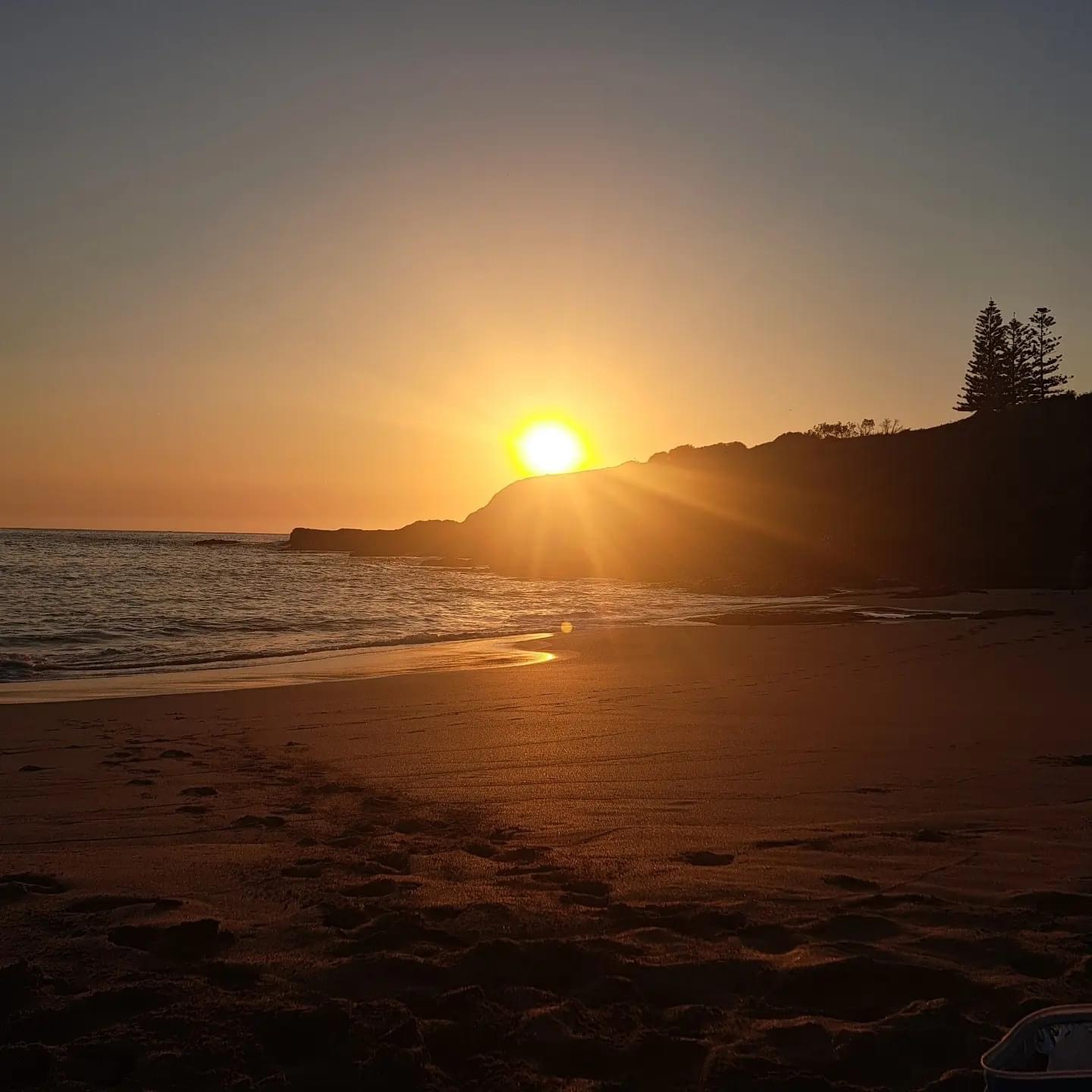 Footprints in the sand leading toward a sunrise over the ocean